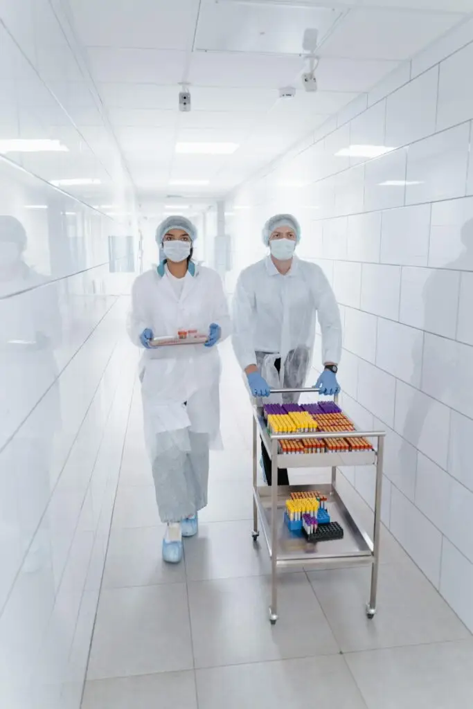 Two lab technicians in protective gear transport samples through a hallway.